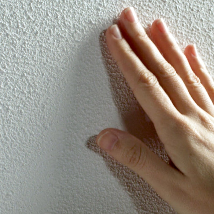 Hand beruehrt frisch gestrichene Wand und fuehlt die Struktur von AlpenKalk Rollputz