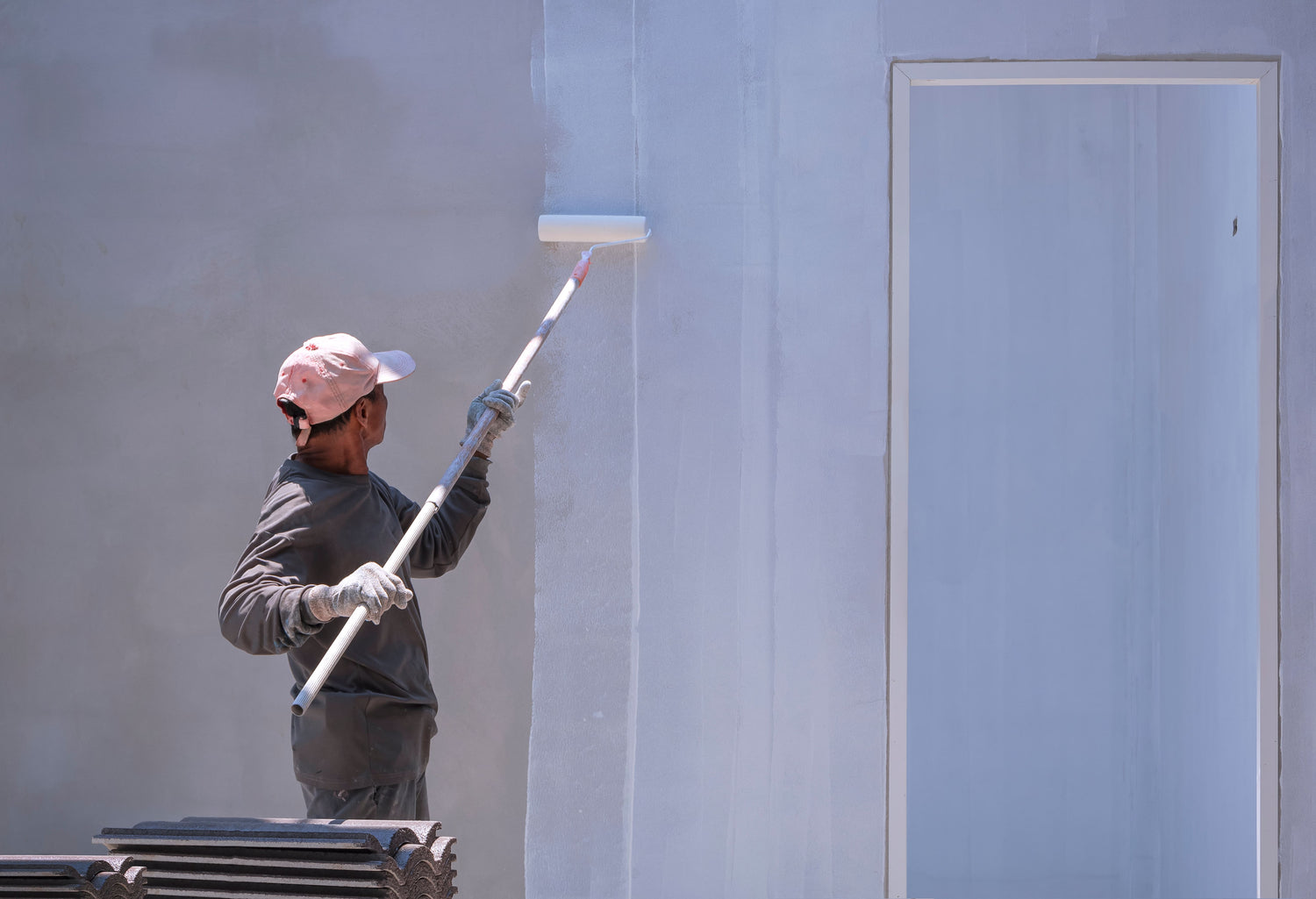 Arbeiter trägt Farbe mit einer Rolle an Aussenwand auf