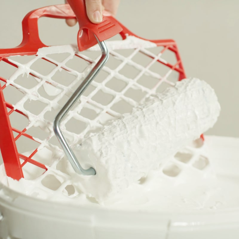 Farbrolle mit Kalkfarbe wird an Abstreifgitter abgestriffen